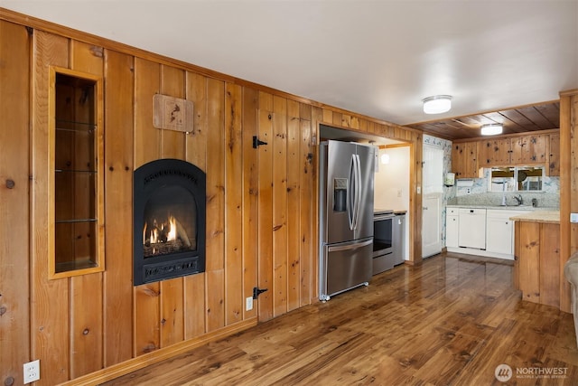 kitchen featuring stainless steel refrigerator with ice dispenser, stove, light countertops, dark wood finished floors, and wooden walls