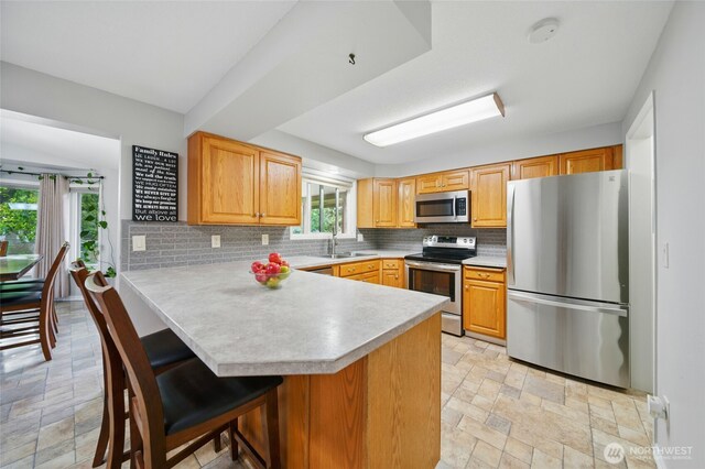 kitchen with stone finish floor, backsplash, appliances with stainless steel finishes, a sink, and light countertops