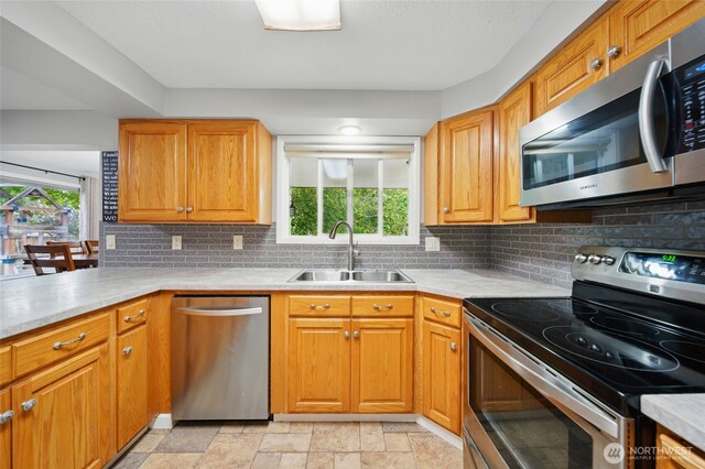kitchen with decorative backsplash, stone finish floor, light countertops, a sink, and appliances with stainless steel finishes