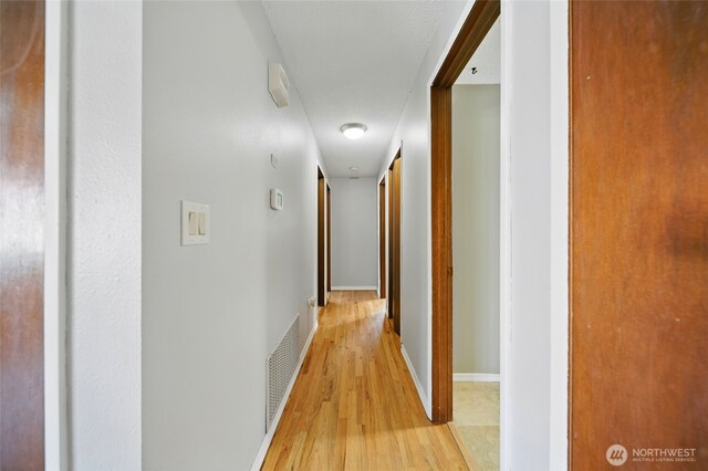 hall with attic access, light wood-style flooring, and visible vents