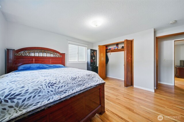 bedroom with a textured ceiling, baseboards, light wood-style flooring, and a closet
