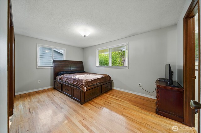 bedroom featuring baseboards, light wood-type flooring, and a textured ceiling
