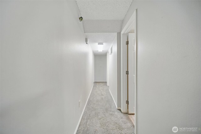hallway featuring carpet floors, a textured ceiling, and baseboards