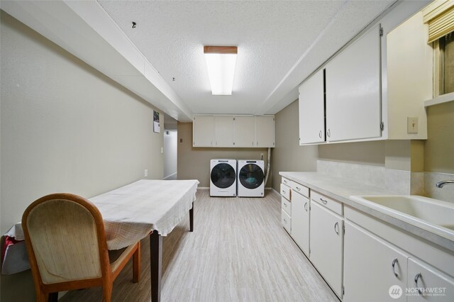 laundry area featuring washing machine and dryer, baseboards, cabinet space, a sink, and light wood-style flooring