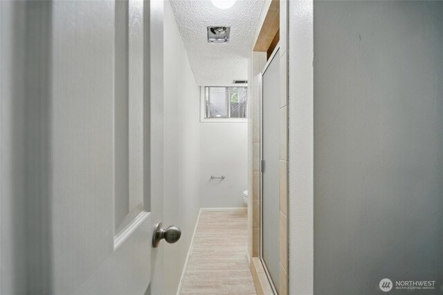 hallway featuring baseboards, a textured ceiling, and wood finished floors
