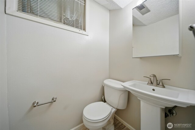 half bathroom with baseboards, toilet, a textured ceiling, and visible vents