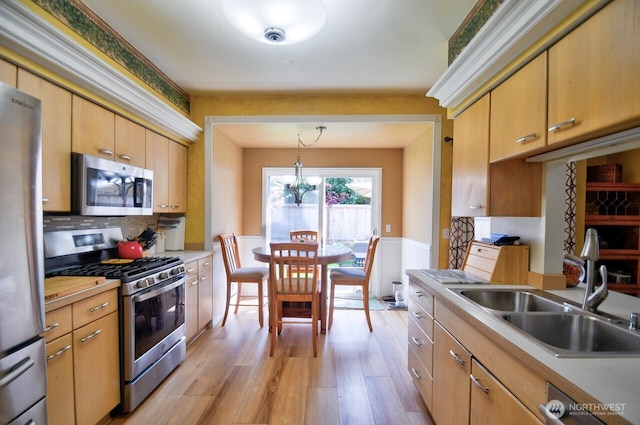 kitchen with stainless steel appliances, light countertops, a sink, light wood-style flooring, and tasteful backsplash