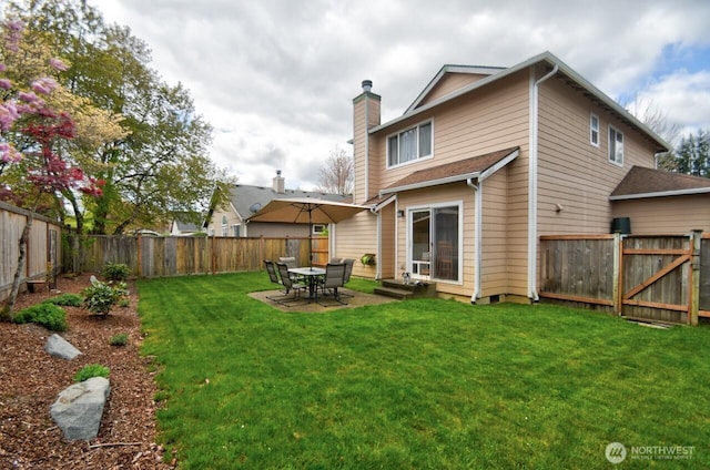 rear view of house with entry steps, a lawn, a fenced backyard, and a chimney