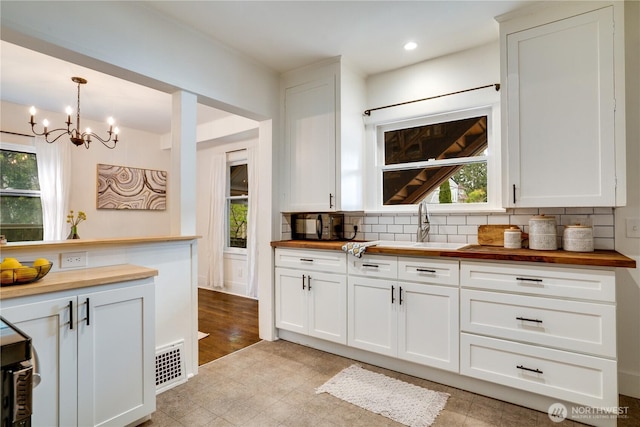 kitchen featuring wood counters, backsplash, a healthy amount of sunlight, and a chandelier