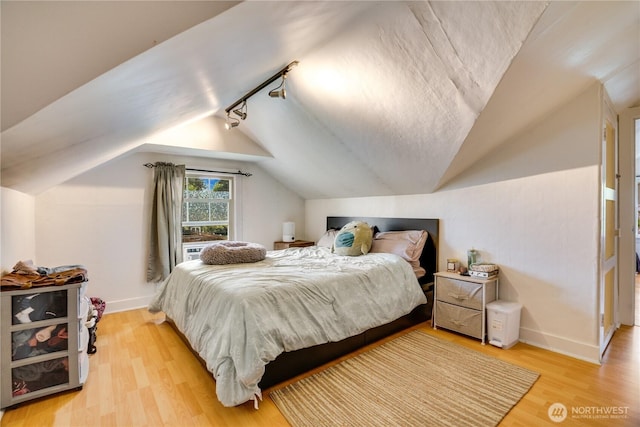 bedroom with light wood-type flooring, baseboards, lofted ceiling, and track lighting