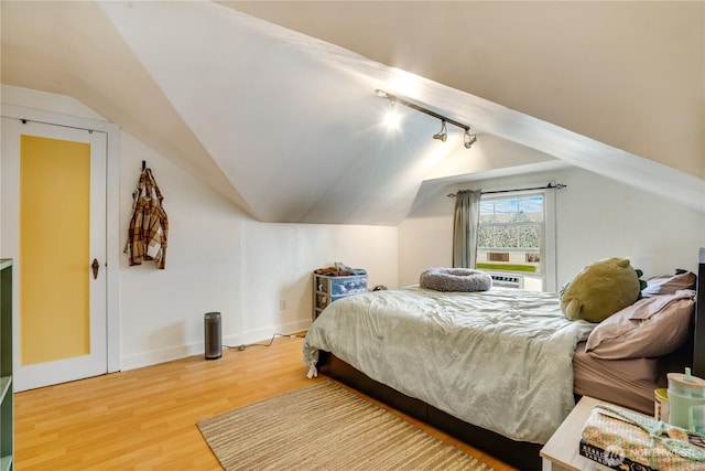 bedroom featuring track lighting, baseboards, wood finished floors, and lofted ceiling