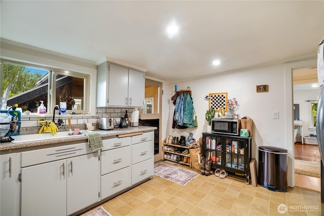 kitchen featuring ornamental molding, light countertops, stainless steel microwave, white cabinets, and a sink