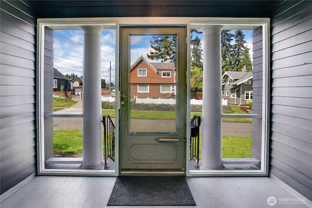 doorway to outside with wooden walls, decorative columns, and wood finished floors