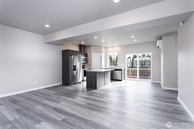 kitchen featuring a center island, wood finished floors, open floor plan, stainless steel appliances, and light countertops