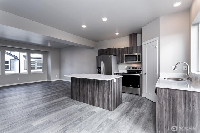 kitchen featuring stainless steel appliances, wood finished floors, modern cabinets, a sink, and a kitchen island