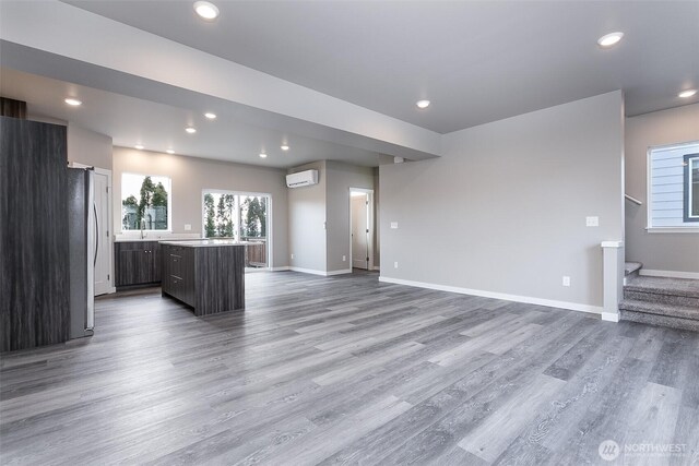 unfurnished living room featuring stairway, wood finished floors, a wall unit AC, baseboards, and recessed lighting