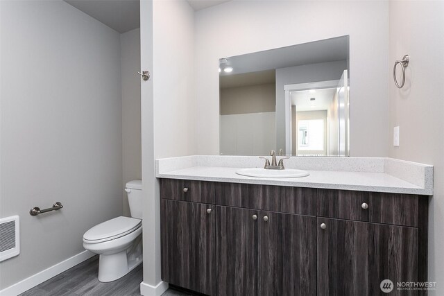 half bathroom with toilet, vanity, wood finished floors, and baseboards
