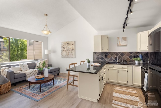 kitchen with rail lighting, dark countertops, a sink, a peninsula, and backsplash