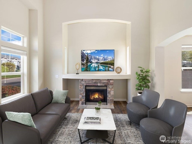 living area with arched walkways, wood finished floors, a towering ceiling, and a fireplace