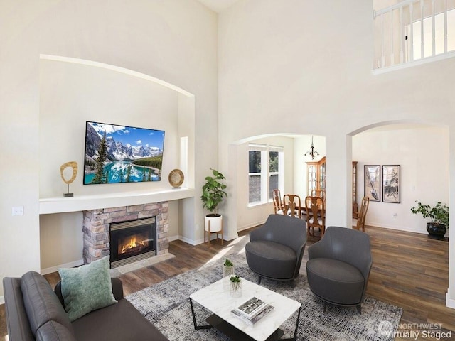 living room featuring a high ceiling, wood finished floors, arched walkways, baseboards, and a fireplace