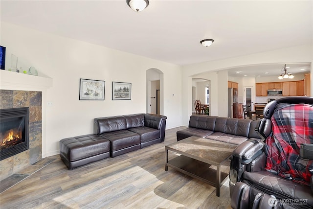 living room with baseboards, arched walkways, light wood finished floors, and a tiled fireplace