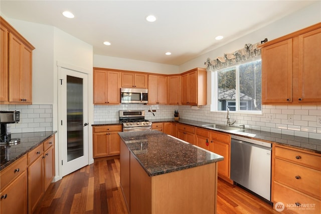 kitchen featuring stainless steel appliances, a center island, dark wood-style floors, a sink, and backsplash