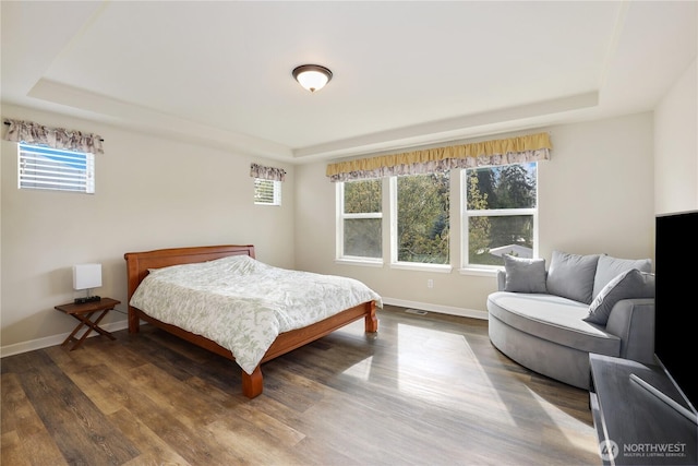 bedroom with a tray ceiling, wood finished floors, and baseboards