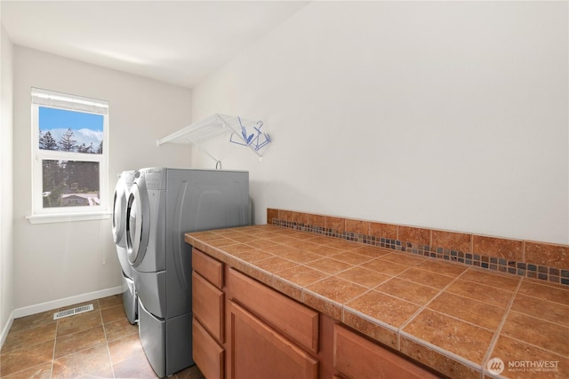 washroom featuring baseboards, visible vents, washer and clothes dryer, and cabinet space