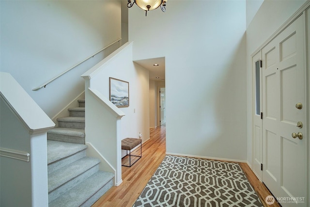 foyer entrance with baseboards, a towering ceiling, wood finished floors, and stairway