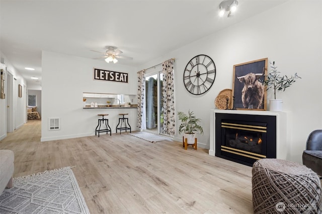 living room with wood finished floors, visible vents, baseboards, a glass covered fireplace, and ceiling fan