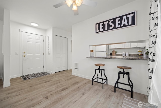 foyer entrance with visible vents, light wood finished floors, baseboards, and a ceiling fan