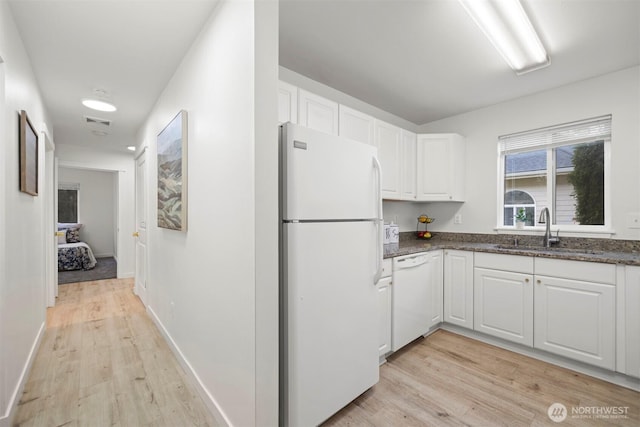 kitchen featuring white cabinets, visible vents, a sink, white appliances, and light wood-style flooring