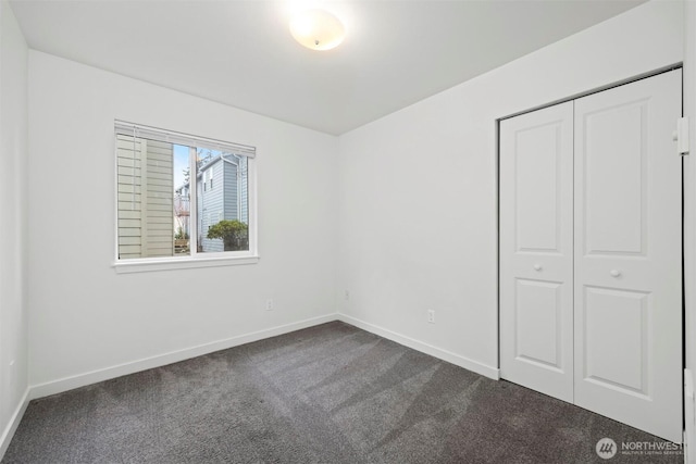 unfurnished bedroom featuring dark colored carpet, baseboards, and a closet