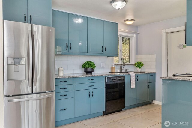 kitchen featuring blue cabinets, decorative backsplash, stainless steel fridge, black dishwasher, and a sink