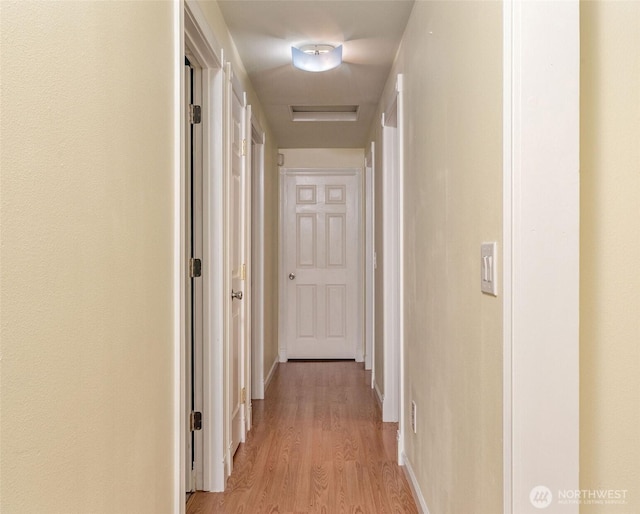 hall featuring baseboards, visible vents, and light wood finished floors