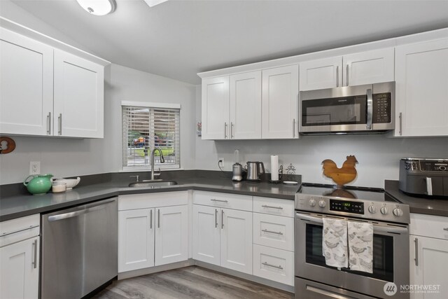 35622 4th Ave SW, Federal Way, WA 98023 - kitchen with white cabinets, dark countertops, a sink, light wood-style flooring, and appliances with stainless steel finishes