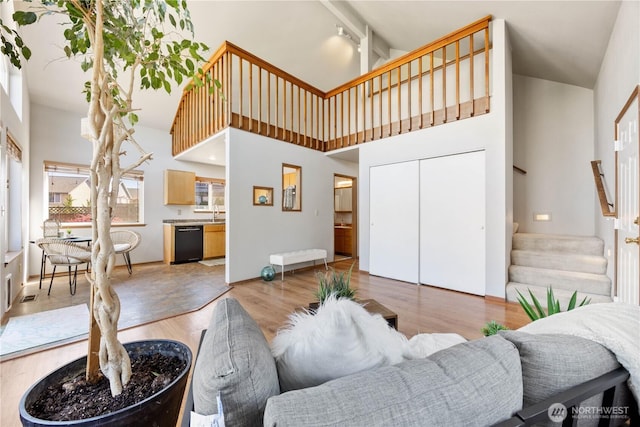 living area featuring stairway, a healthy amount of sunlight, light wood-style floors, and high vaulted ceiling