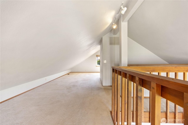interior space with track lighting, vaulted ceiling, baseboards, and light carpet
