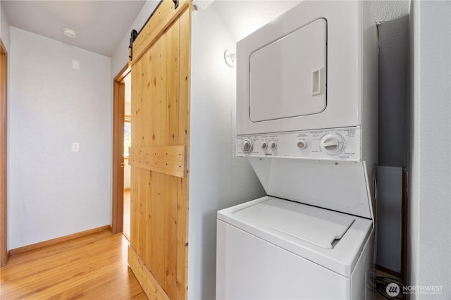 washroom featuring stacked washer and dryer, a barn door, baseboards, light wood-style floors, and laundry area