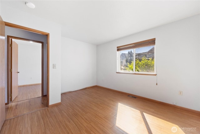 empty room featuring wood finished floors, visible vents, and baseboards