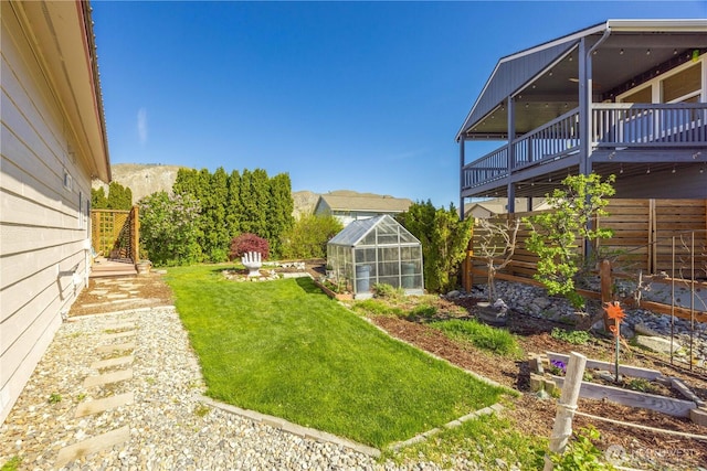 view of yard featuring an outdoor structure, a garden, a deck with mountain view, and a greenhouse