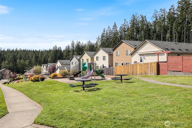 surrounding community featuring a residential view, a playground, fence, a lawn, and a forest view