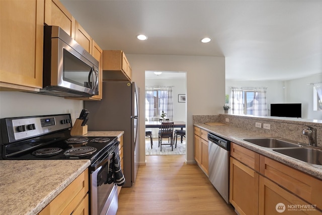 kitchen featuring light wood finished floors, stainless steel appliances, a sink, light brown cabinets, and light countertops