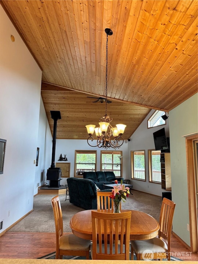 carpeted dining area featuring wooden ceiling, an inviting chandelier, baseboards, a wood stove, and high vaulted ceiling