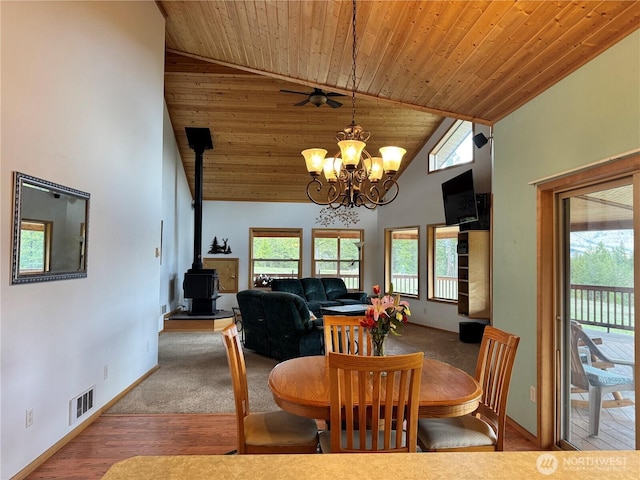 dining space featuring a wood stove, a notable chandelier, high vaulted ceiling, visible vents, and baseboards