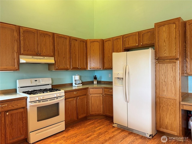 kitchen featuring brown cabinetry, light wood finished floors, under cabinet range hood, and white appliances
