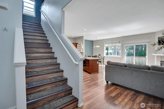 stairway with recessed lighting, wood finished floors, an inviting chandelier, and a fireplace