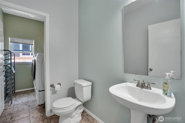 bathroom with stone finish floor, toilet, a sink, baseboards, and washer / clothes dryer