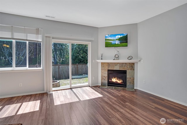 unfurnished living room with wood finished floors, a tiled fireplace, visible vents, and baseboards