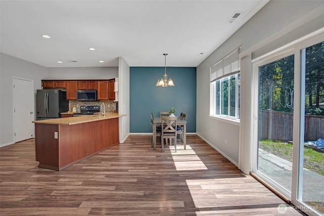 kitchen with range with electric cooktop, stainless steel microwave, freestanding refrigerator, a peninsula, and brown cabinetry